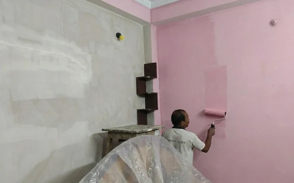 Service Square painter applying pink emulsion paint with a roller on an interior bedroom wall in Chennai