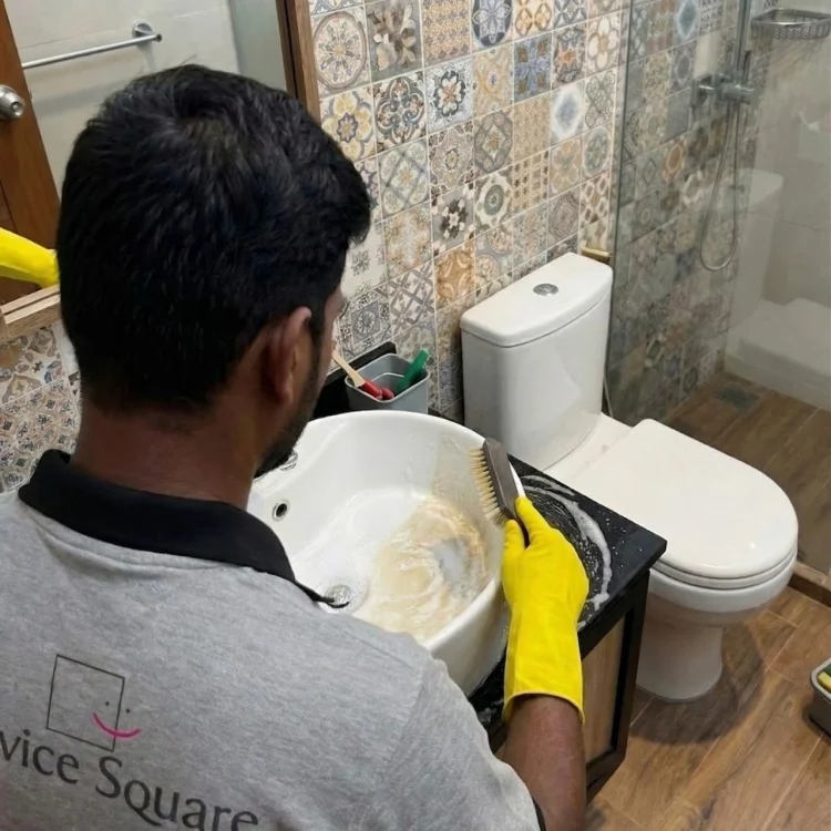 Service Square technician scrubbing a bathroom washbasin and vanity countertop next to a toilet in Chennai